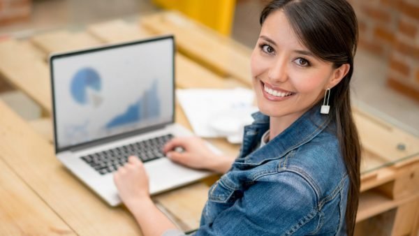 Happy woman working at the office using her laptop and looking at the camera smiling